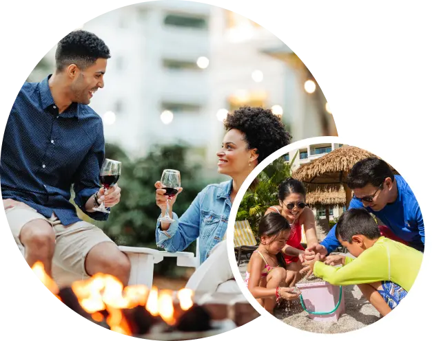 Couple holding wine glasses and family playing in the sand